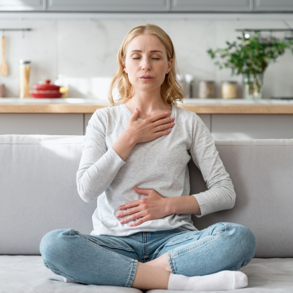 A woman sitting on the couch with her hands on her chest, focusing on blood circulation.