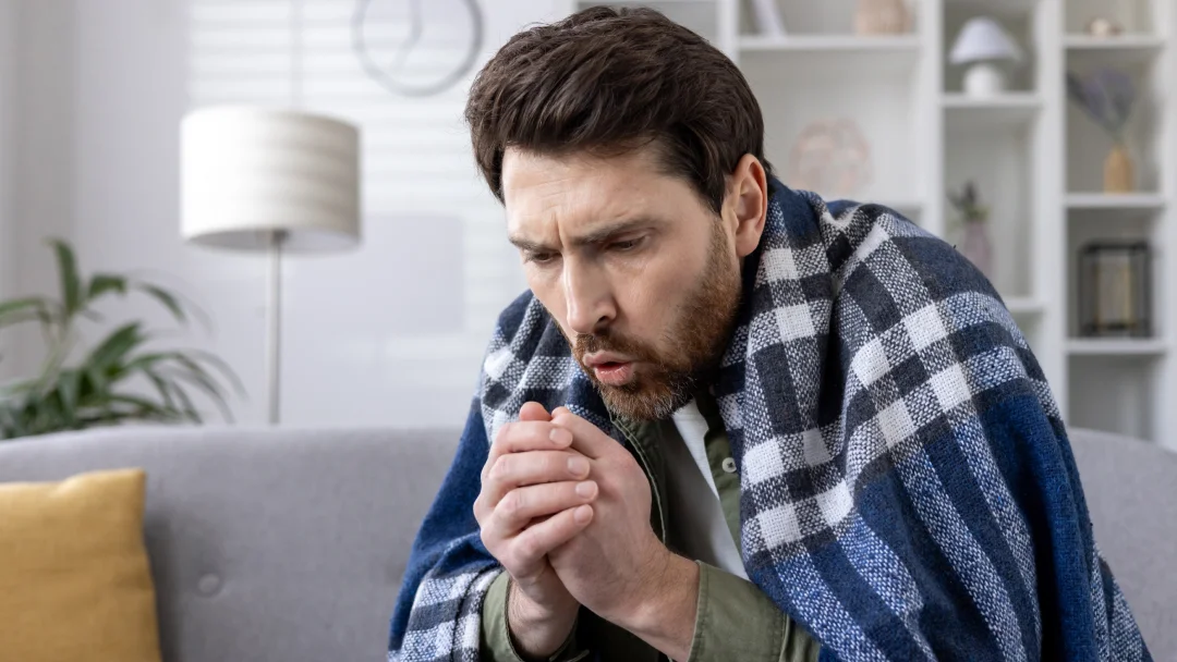 A man sits on a couch, hands on his face, reflecting the fatigue often associated with anemia and iron deficiency.