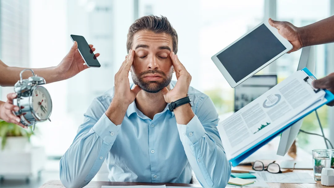 Un homme avec ses mains sur sa tête à son bureau, réfléchissant à des techniques efficaces de gestion du stress pour le syndrome de Raynaud.