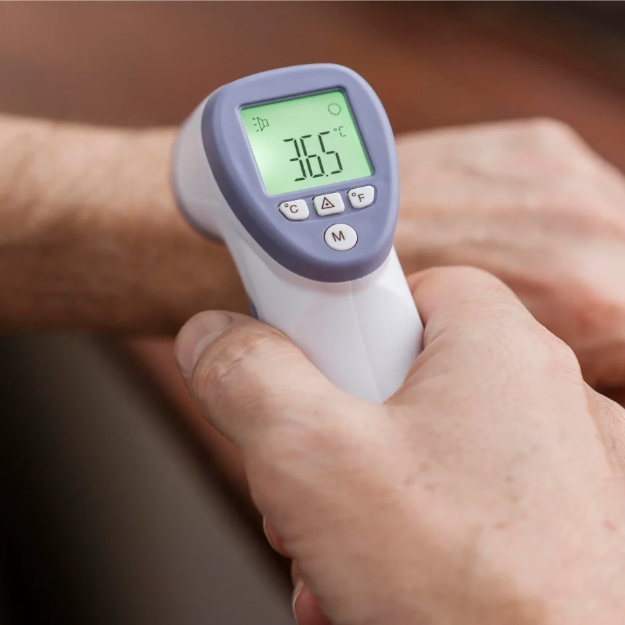 Une personne tient un thermomètre électronique dans sa main, les mains visiblement froides.