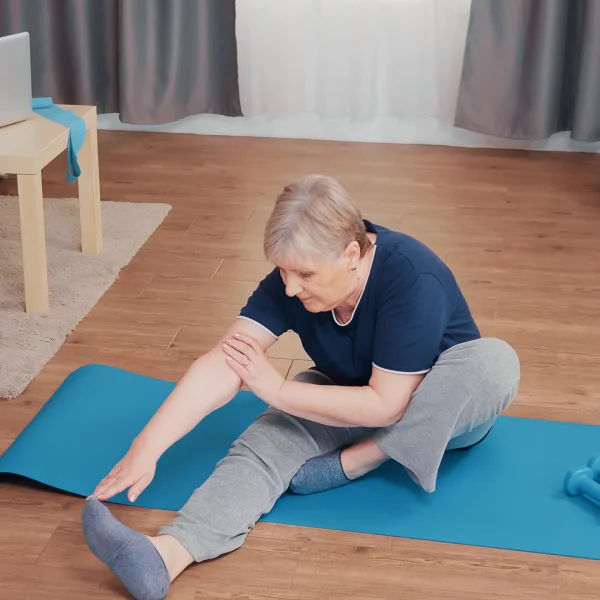 An older woman is performing a stretching exercise on a yoga mat, focusing on her flexibility and balance.