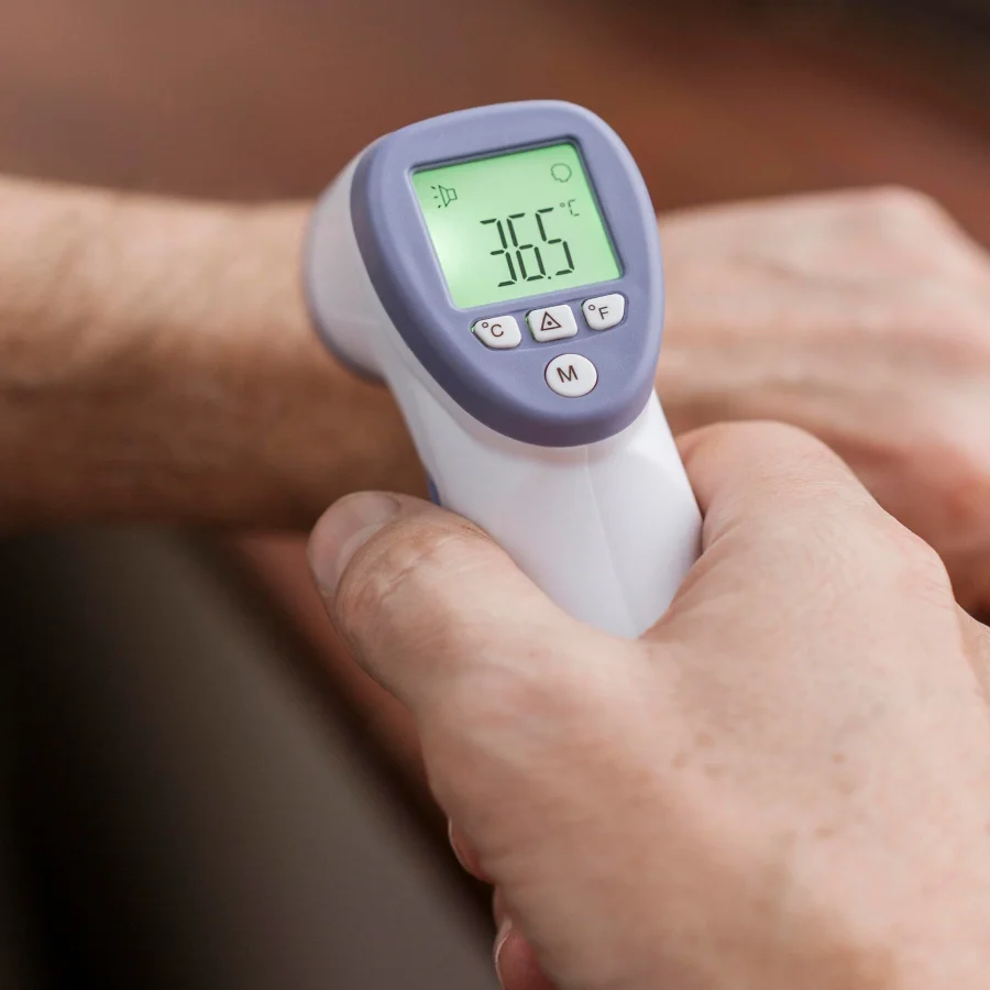 A person with cold hands holds an electronic thermometer, preparing to check their temperature.