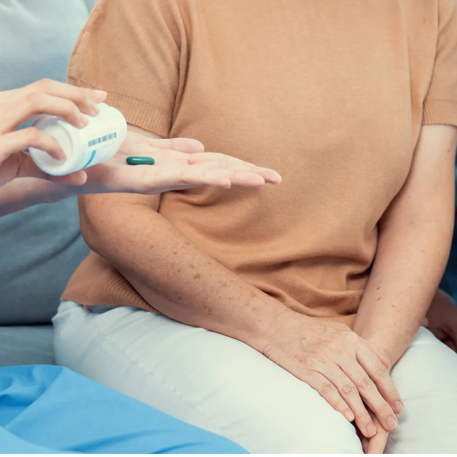 A woman holds a pill while a man sits beside her, both discussing Raynaud's disease treatment options.