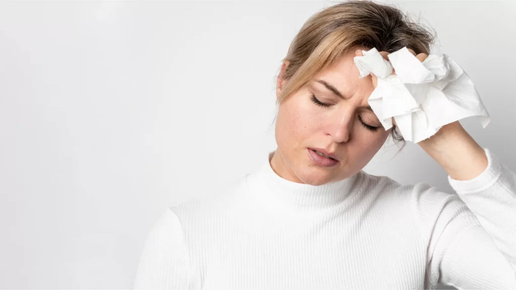 A woman with a cold head, holding a tissue, illustrating symptoms of Raynaud's disease.