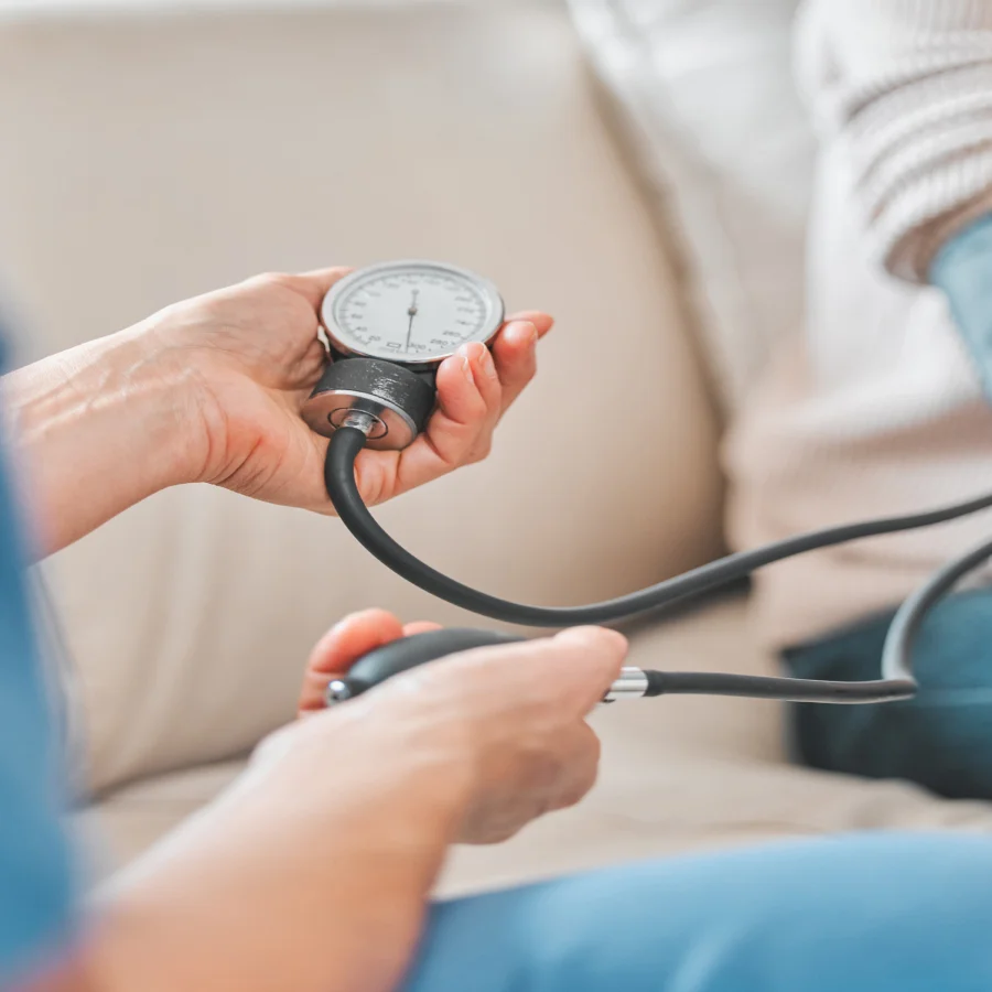 A person sitting on a couch checks their blood pressure with a meter, their hand appears numb.